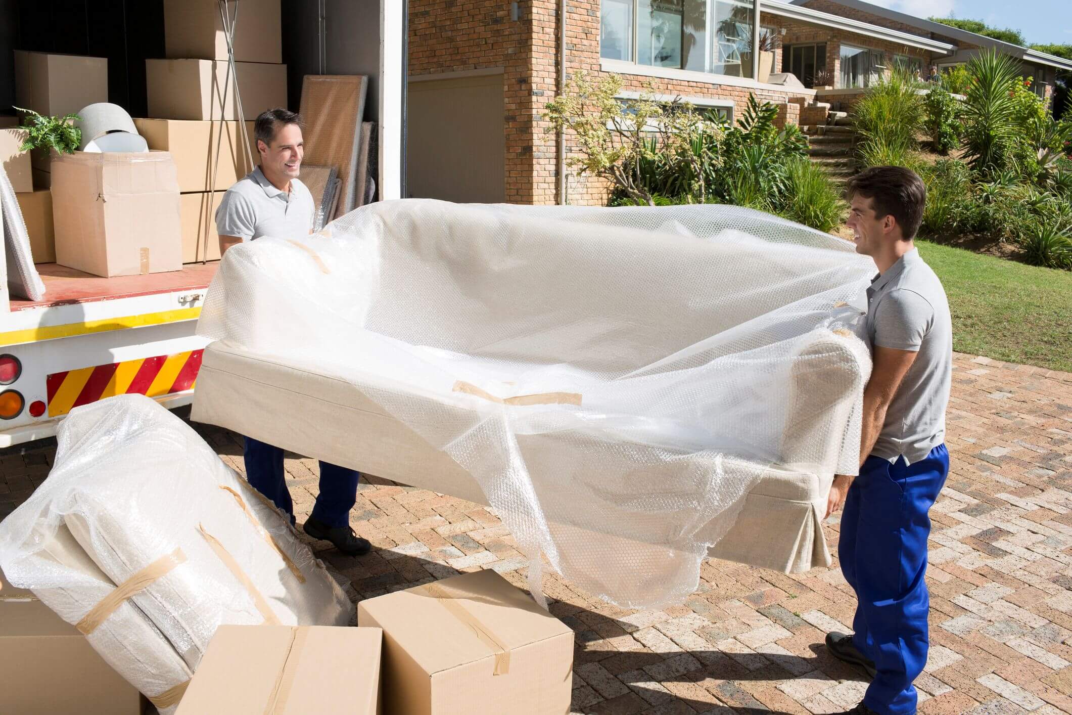 Two movers carrying wrapped couch outside truck.